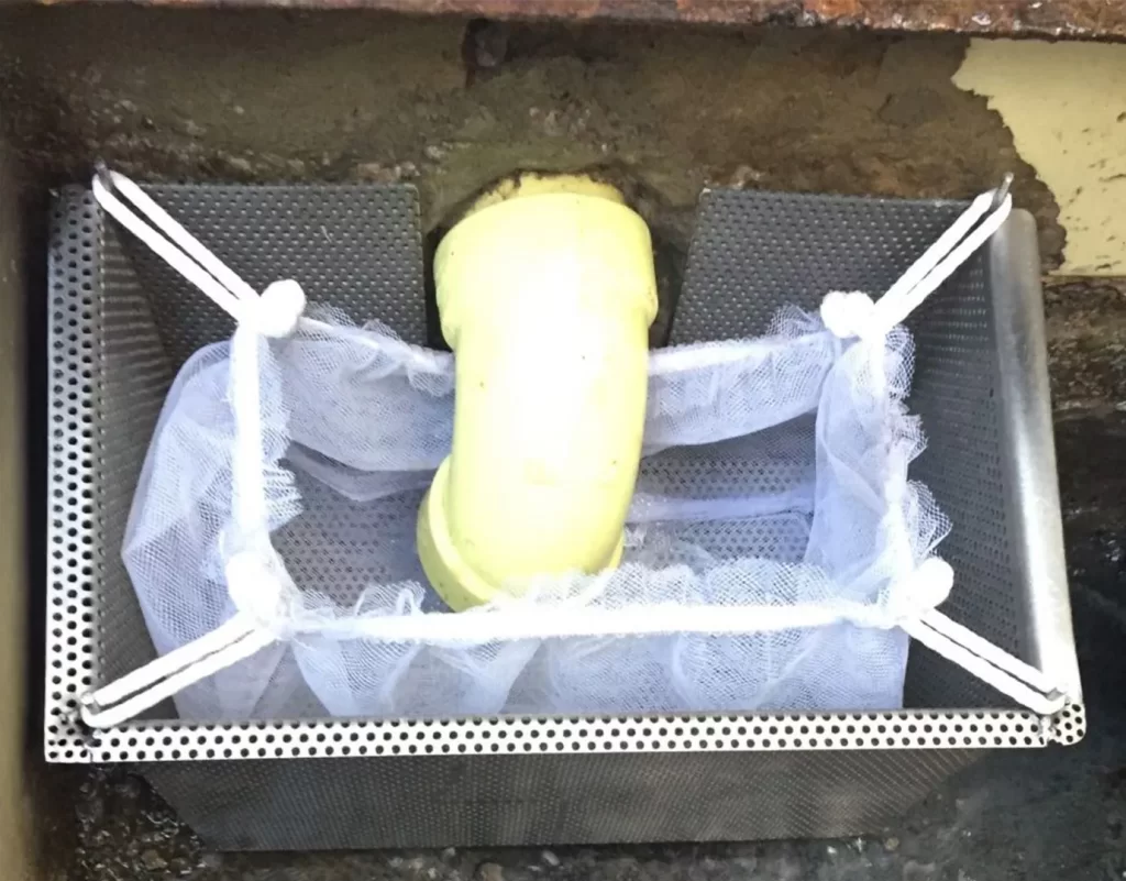 Canastilla de sólidos en acero inoxidable con bolsa filtrante instalada en punto de descarga para retención de residuos gruesos.